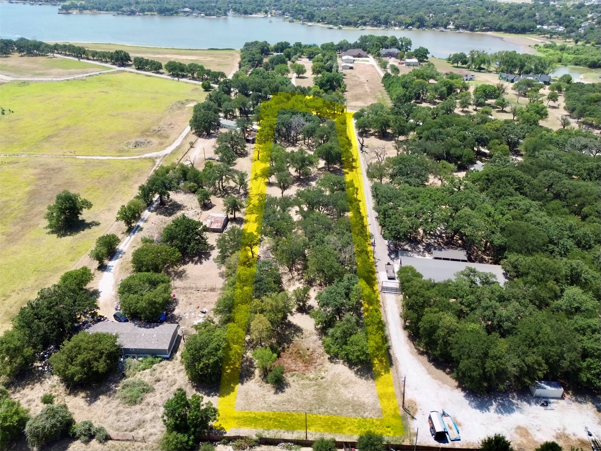 Wooded property lot outlined in yellow, with a road beside it and a lake in the distance.