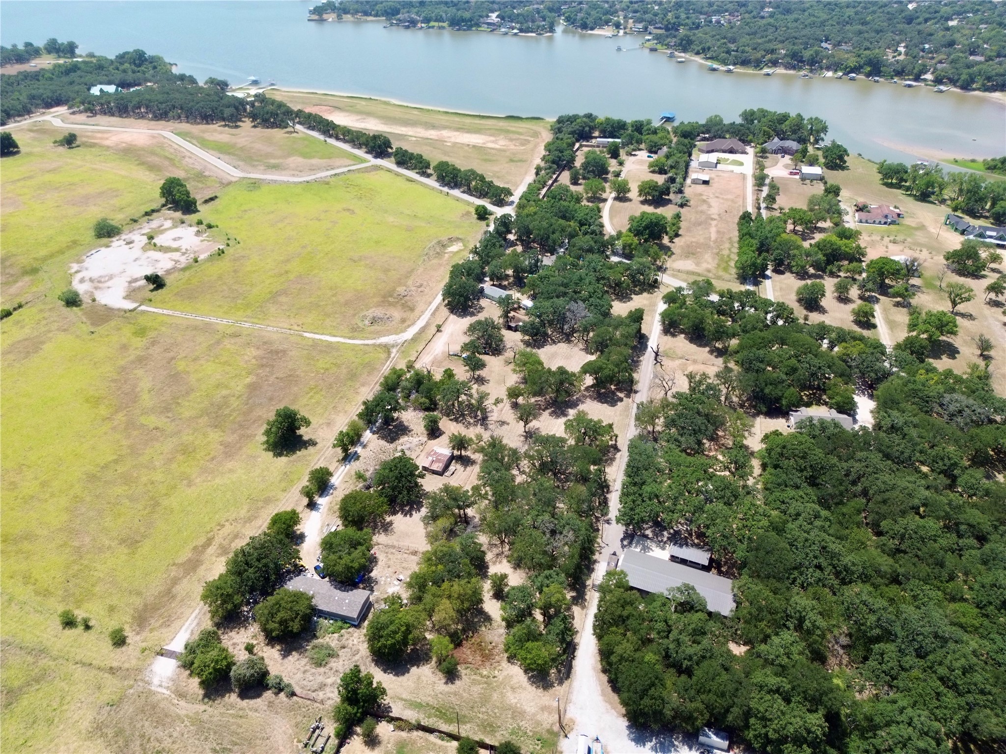 Aerial view of homes and open fields beside a tree-lined lake.