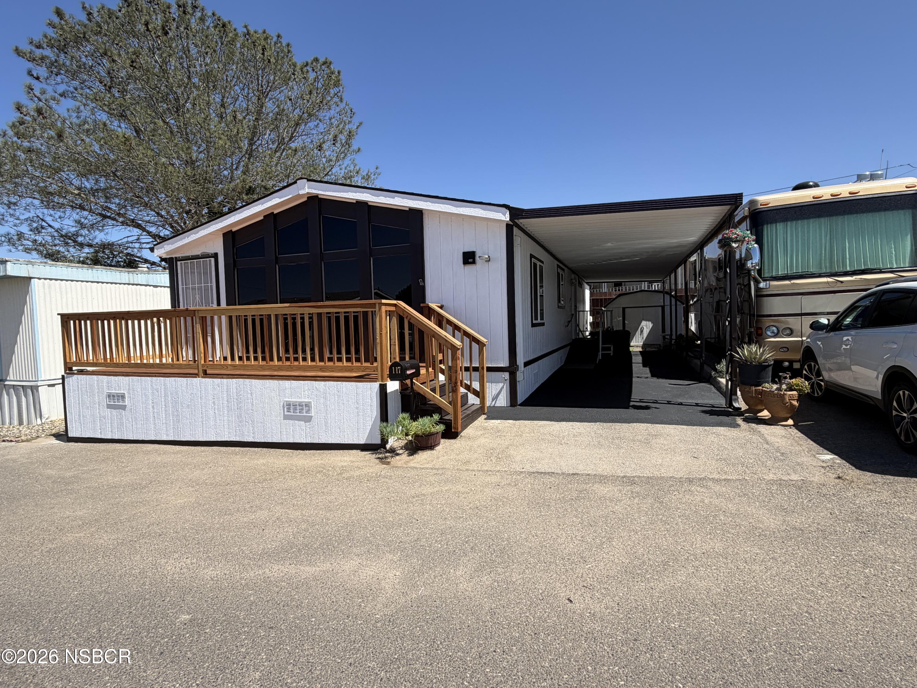 Manufactured home with a raised wooden porch and a covered driveway beside a parked RV.