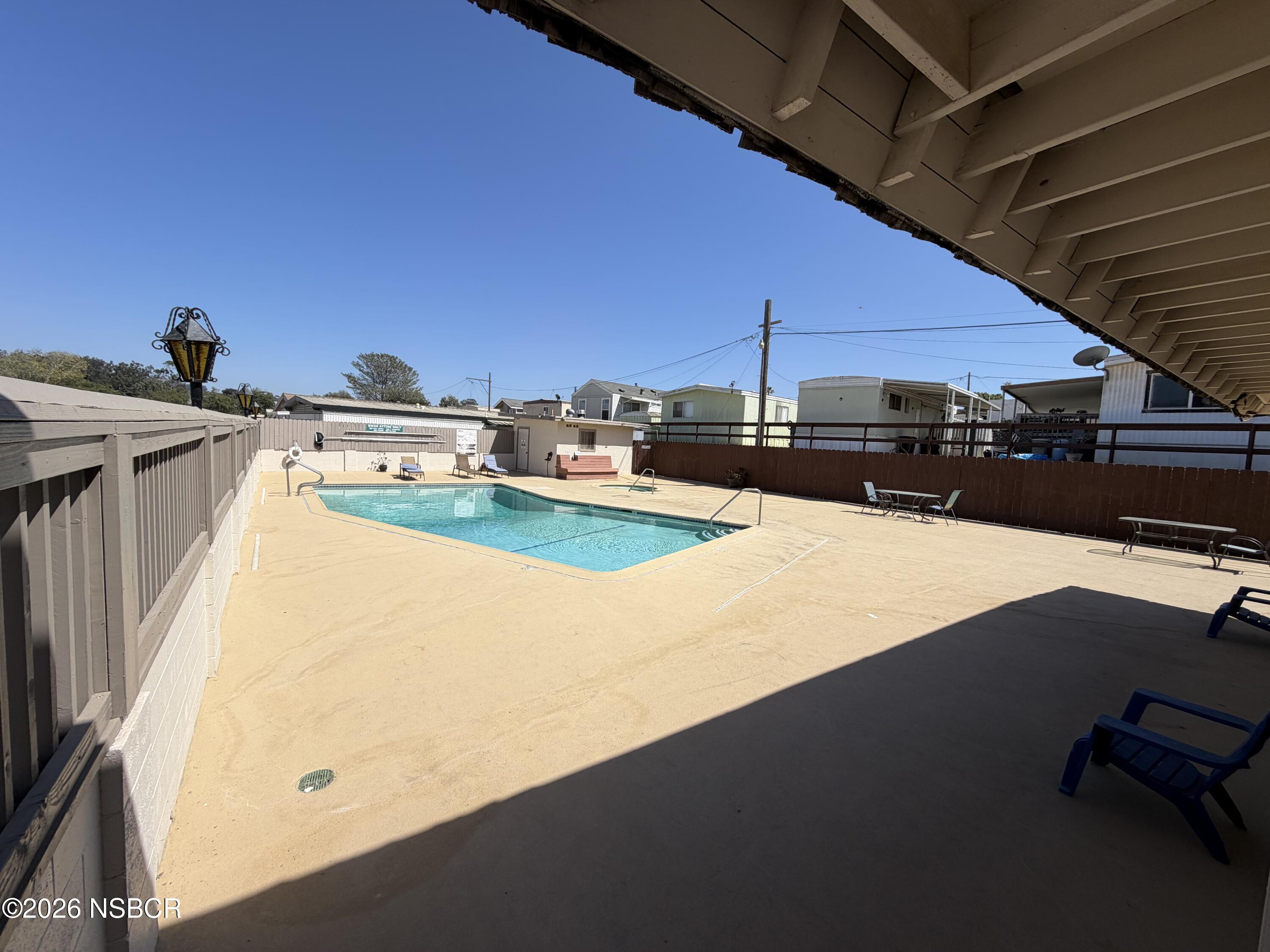 Outdoor swimming pool with a wide concrete deck, lounge chairs, and surrounding fence.
