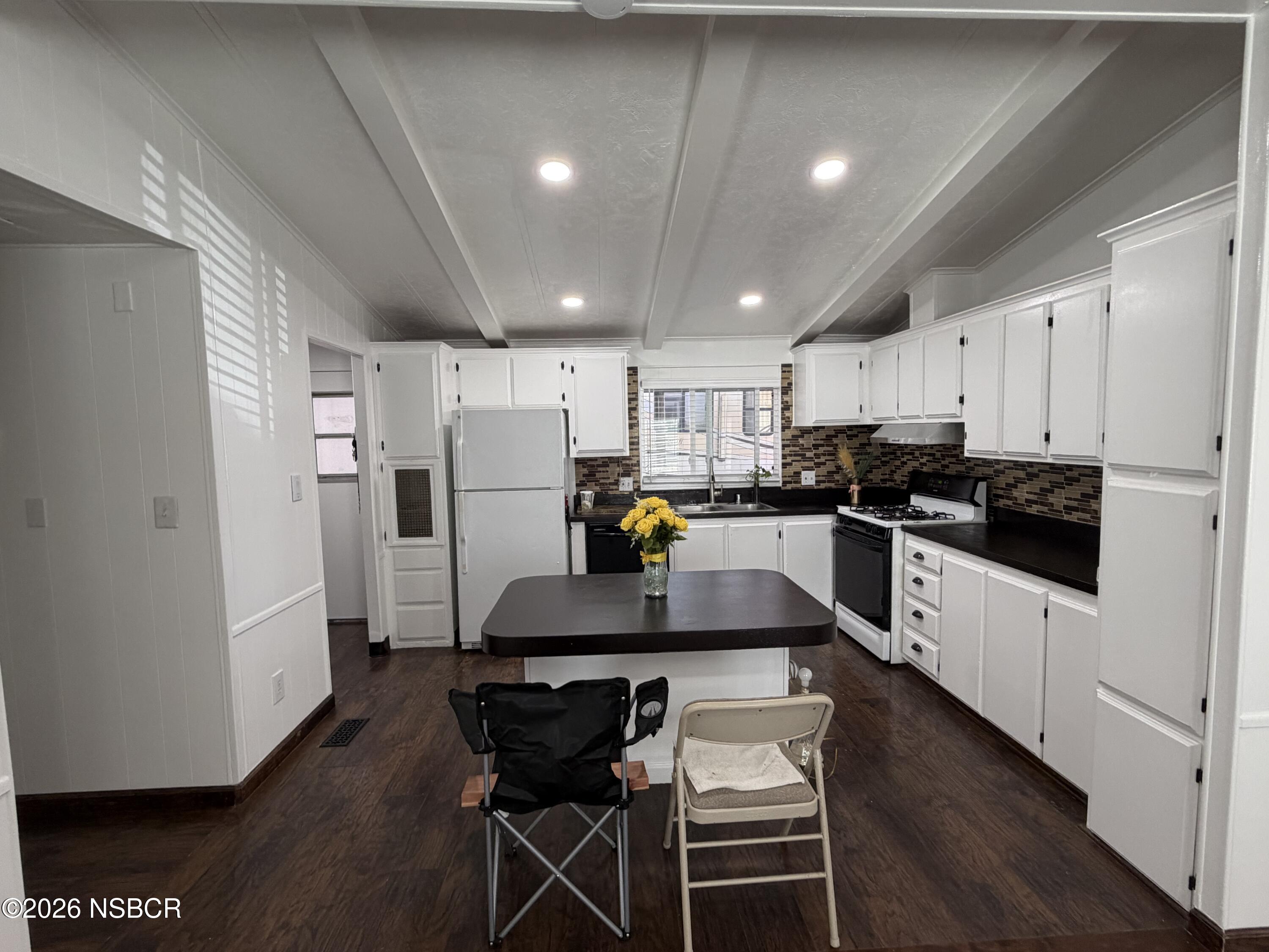 Kitchen with white cabinets, dark counters, tiled backsplash, and an island with yellow flowers.