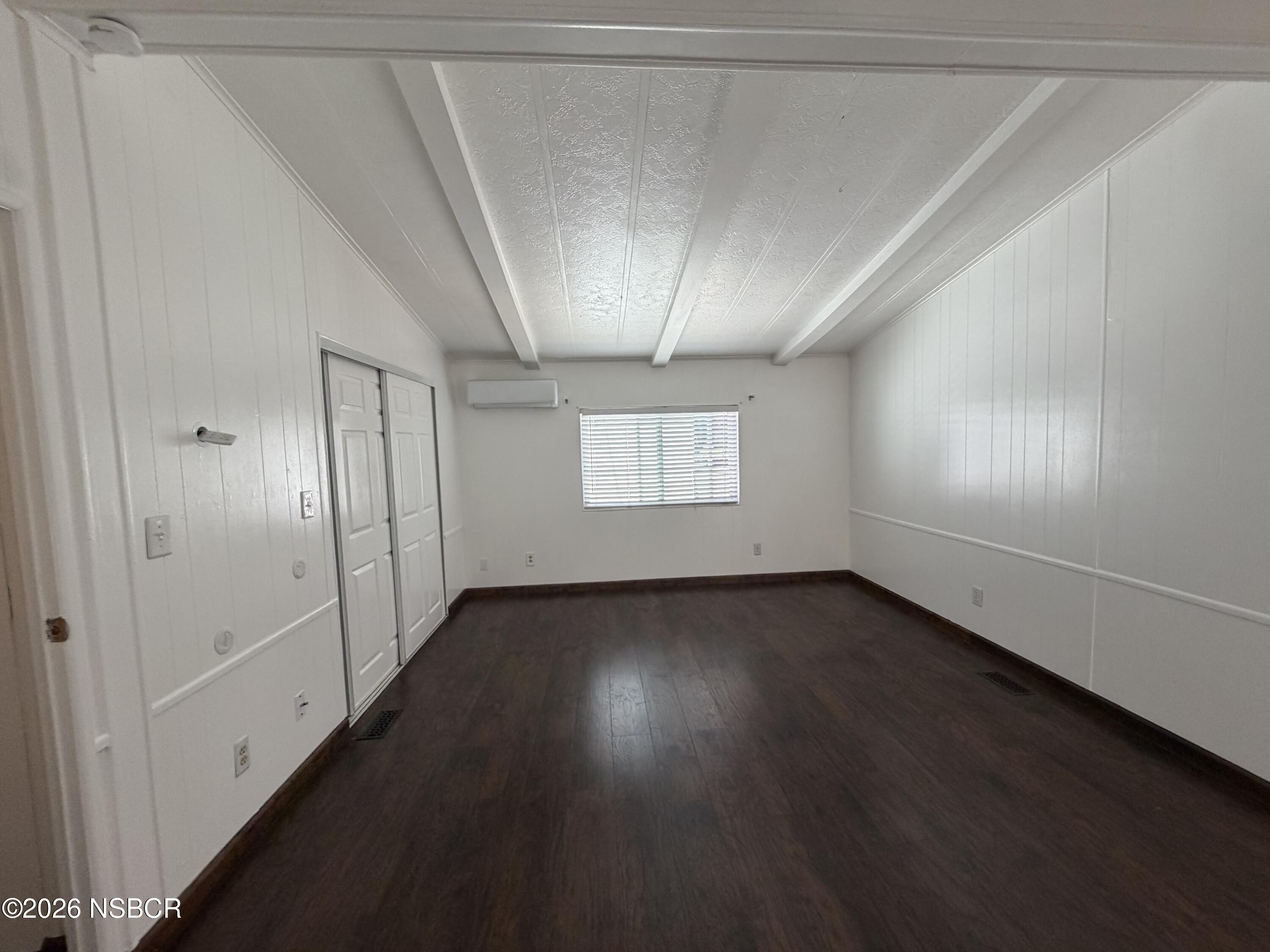 Empty room with dark flooring, sliding closet doors, and a window with blinds.