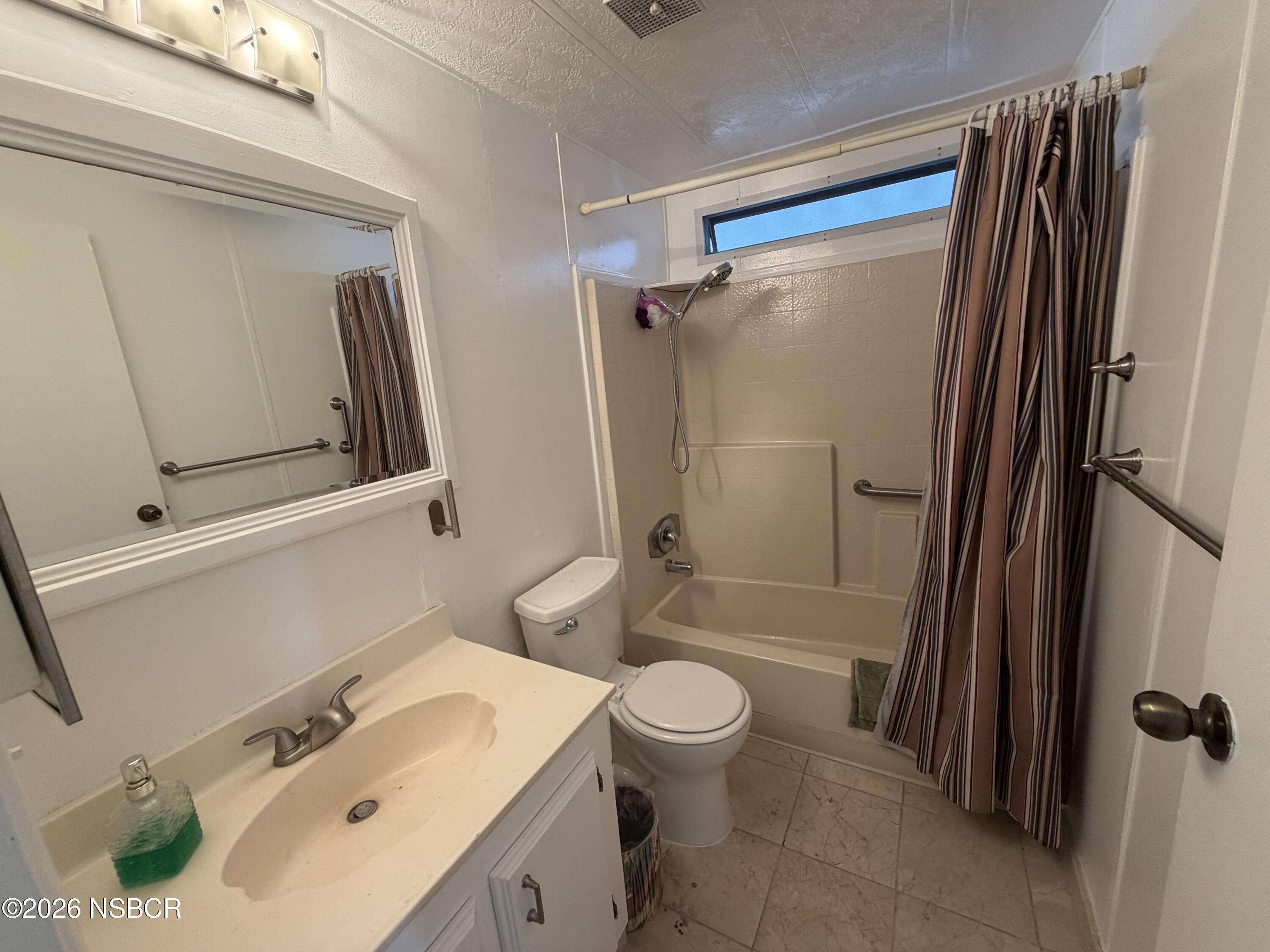 Bathroom with a vanity, toilet, and tub-shower behind a striped curtain.