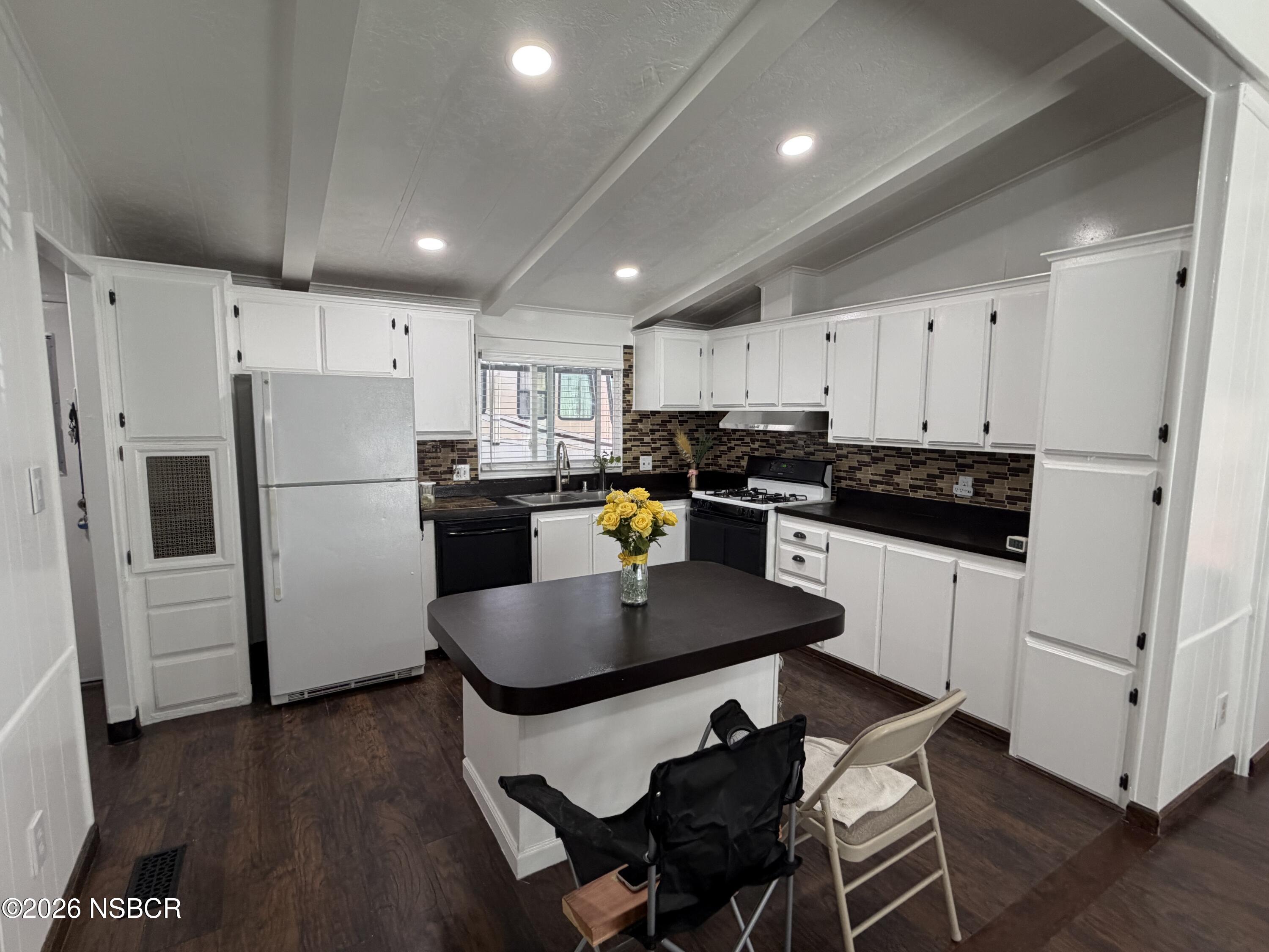 Kitchen with white cabinets, dark counters, and an island topped with yellow roses.