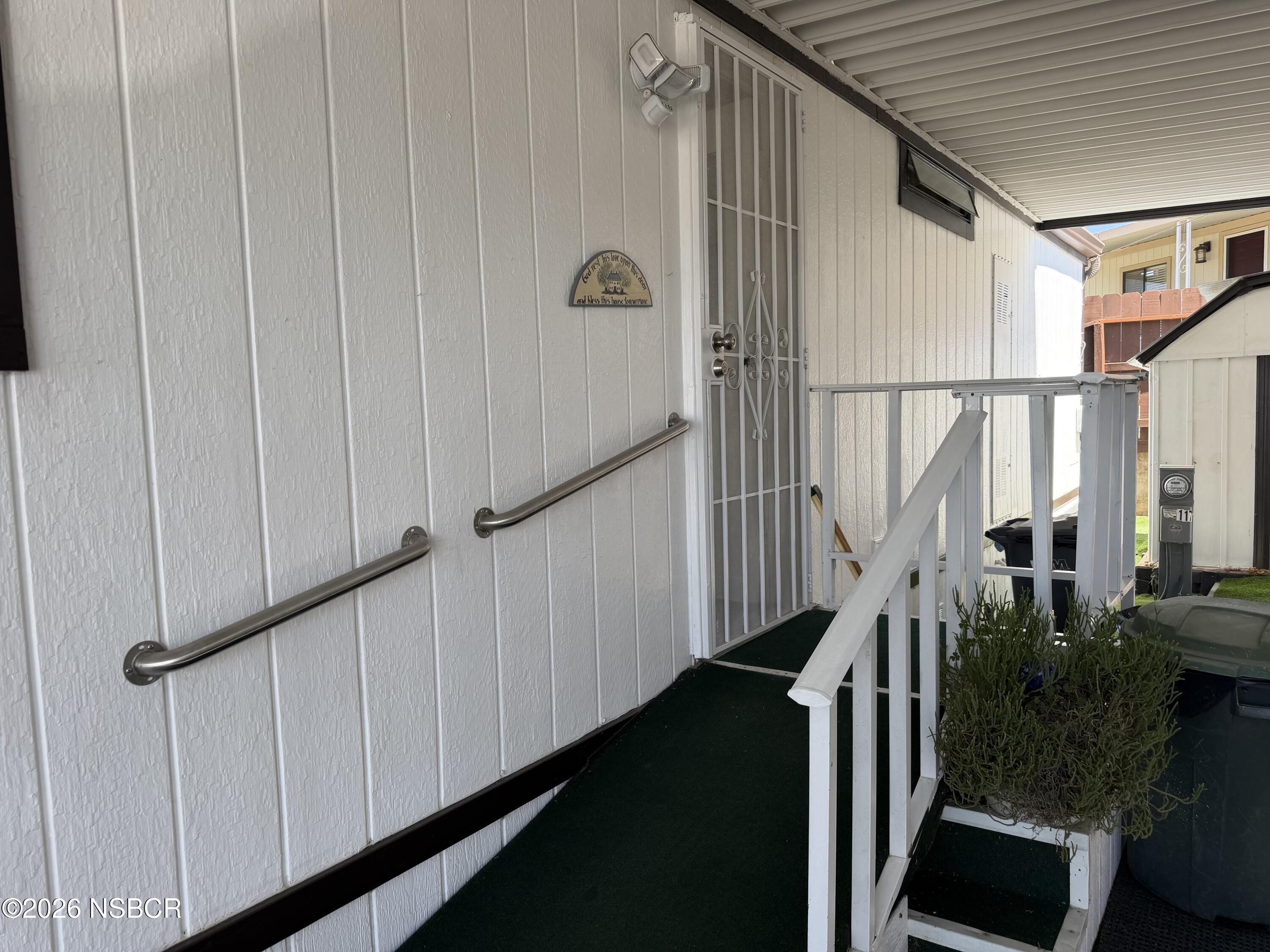 Covered entry walkway with grab bars, white railings, and a metal security screen door.