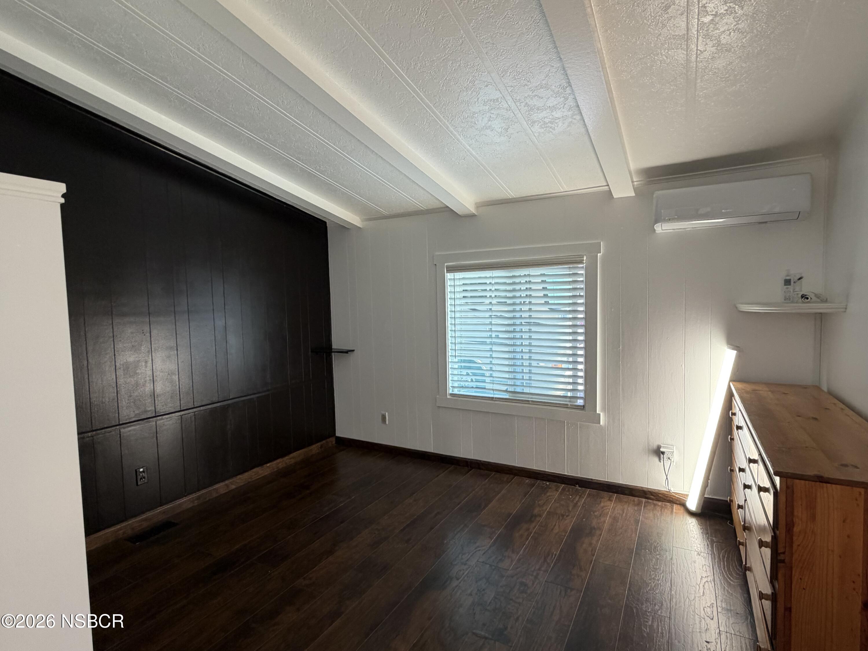 Room with dark wood floors, black paneled wall, window blinds, and wooden dresser.