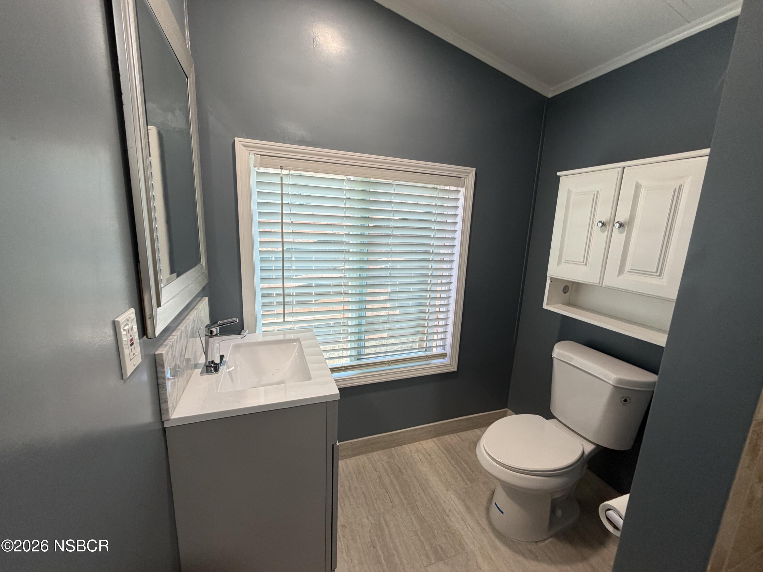 Bathroom with a white vanity and toilet, a wide window with blinds, and dark gray walls.