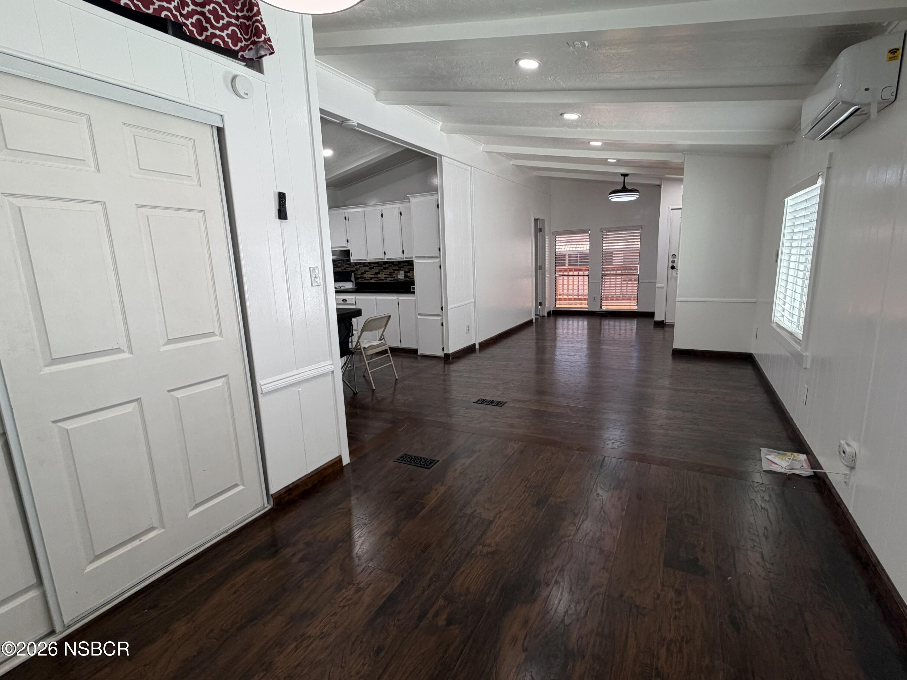 Open living and dining area with dark wood floors, white kitchen cabinets, and a beamed ceiling.