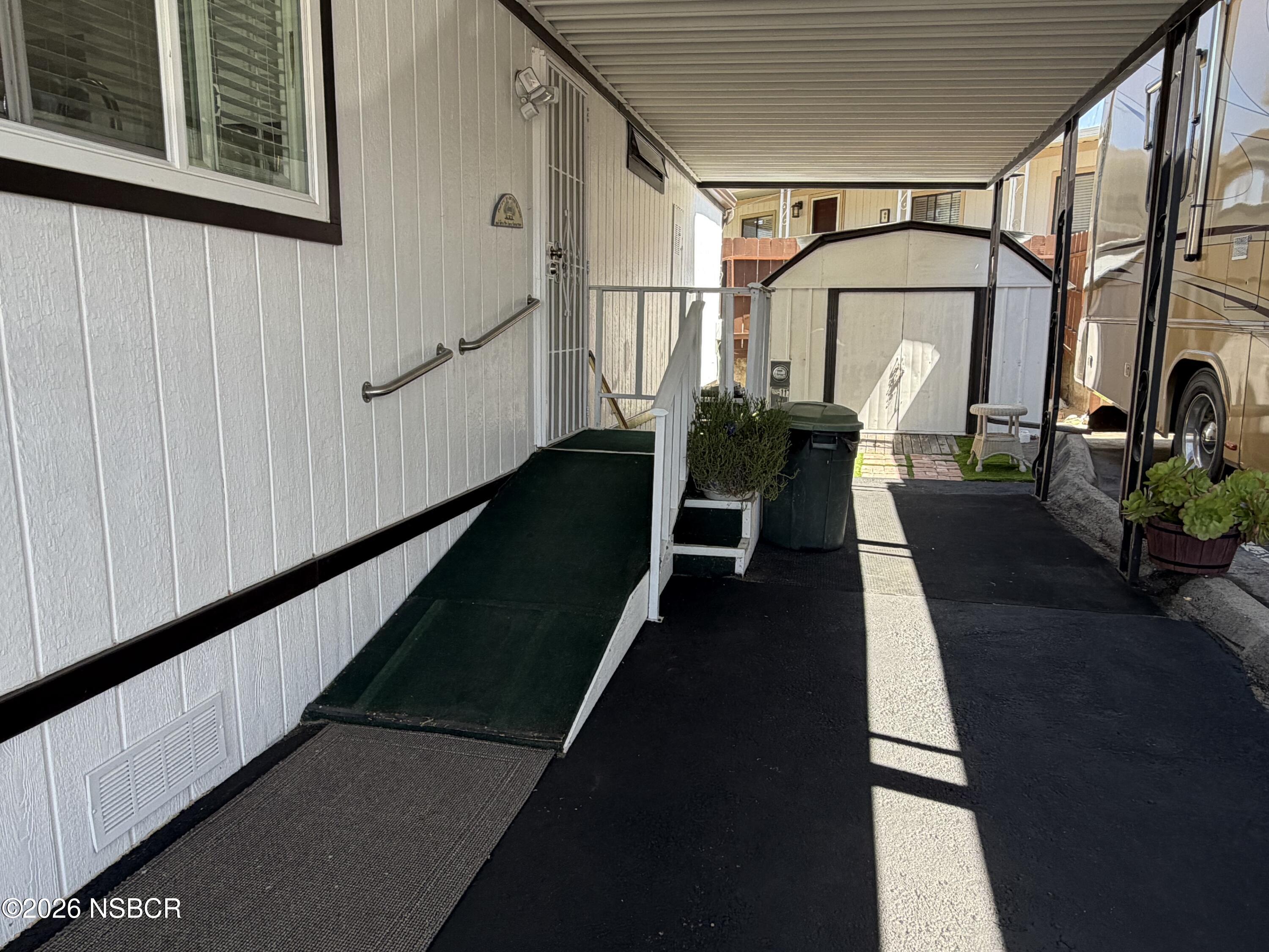 Covered walkway and access ramp beside a manufactured home, with handrails and a storage shed.
