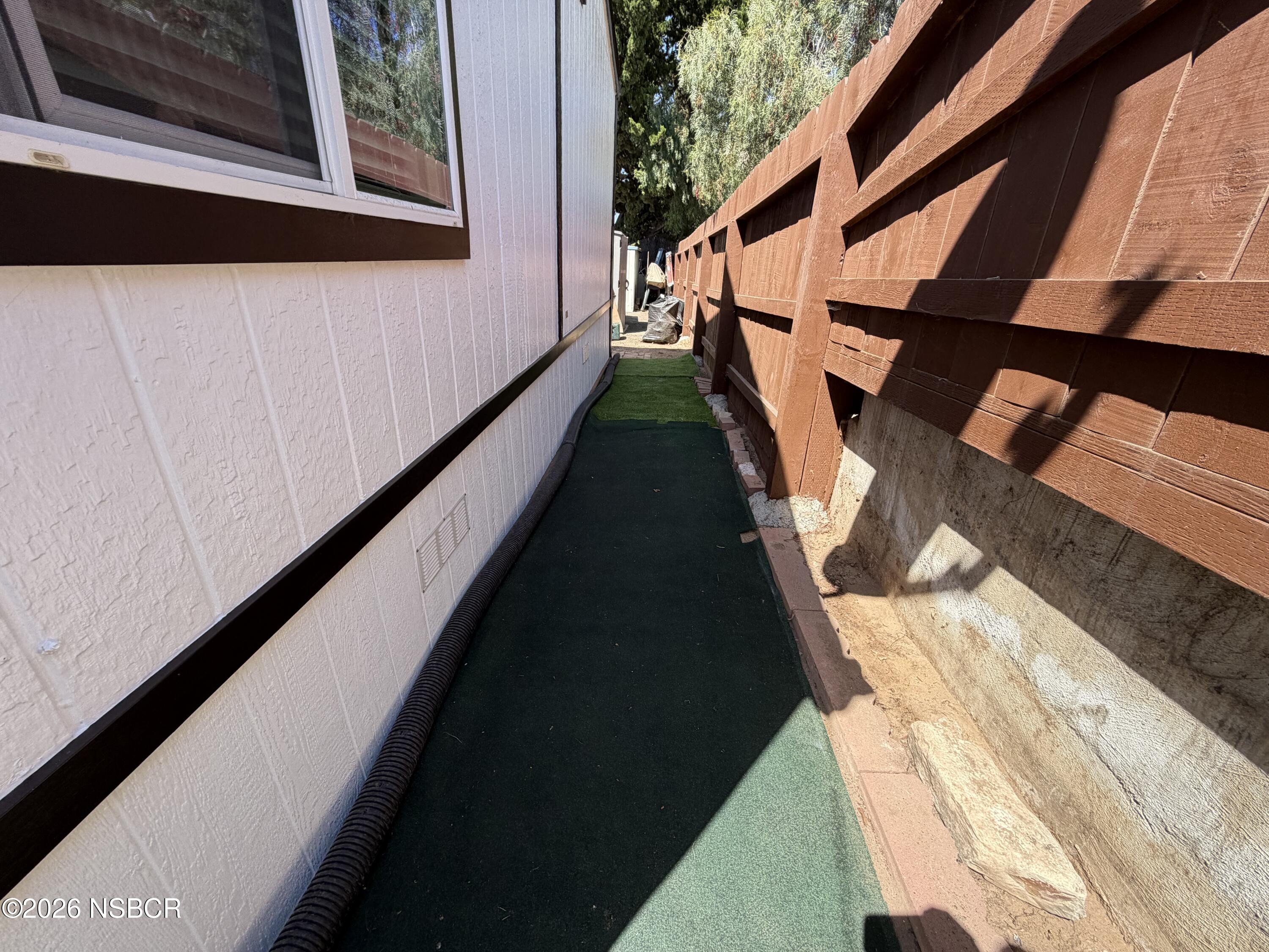 Narrow side yard with artificial turf beside a home and tall wooden fence.