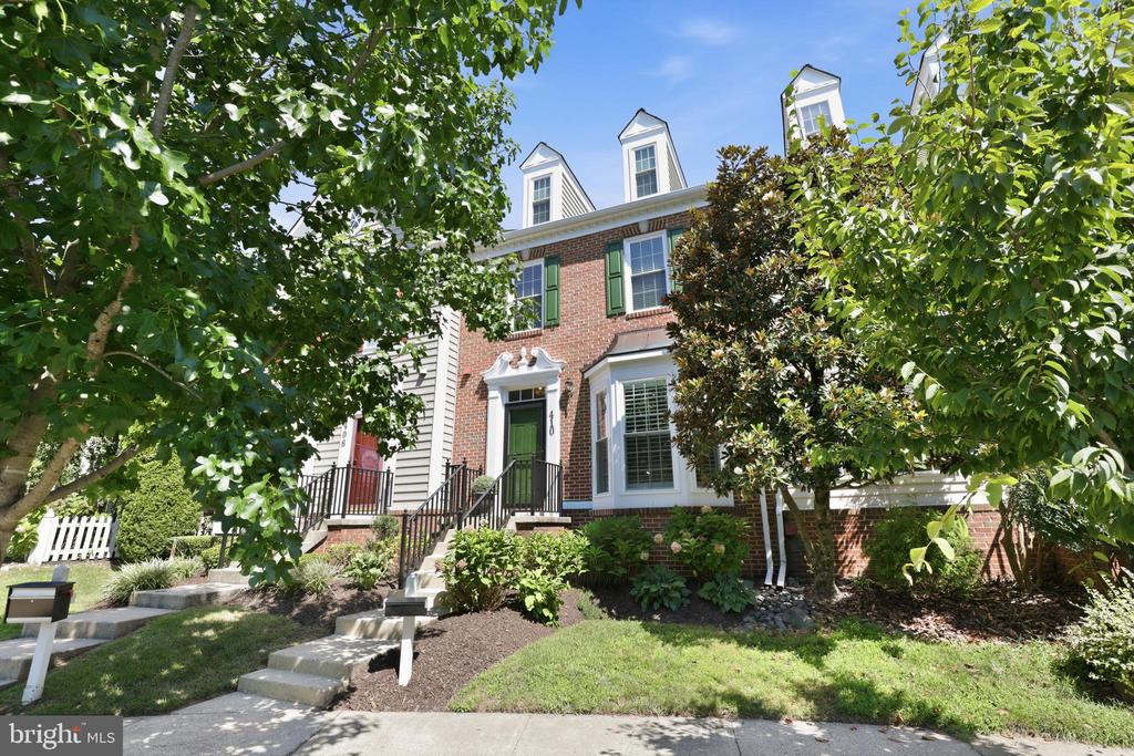 Brick townhouse with green shutters and dormer windows, framed by mature trees and a landscaped garden.