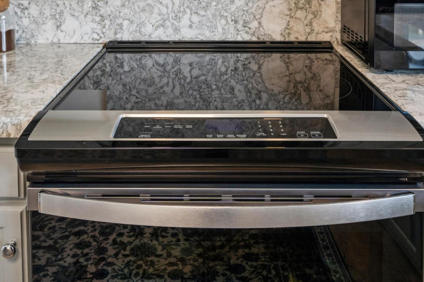 Induction range with a black glass cooktop, stainless-steel handle, and marble backsplash.