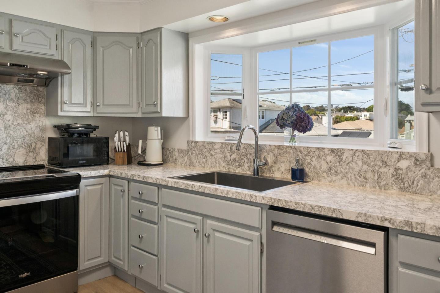 Kitchen with gray cabinets, marble-pattern counters, and a large window above the sink.