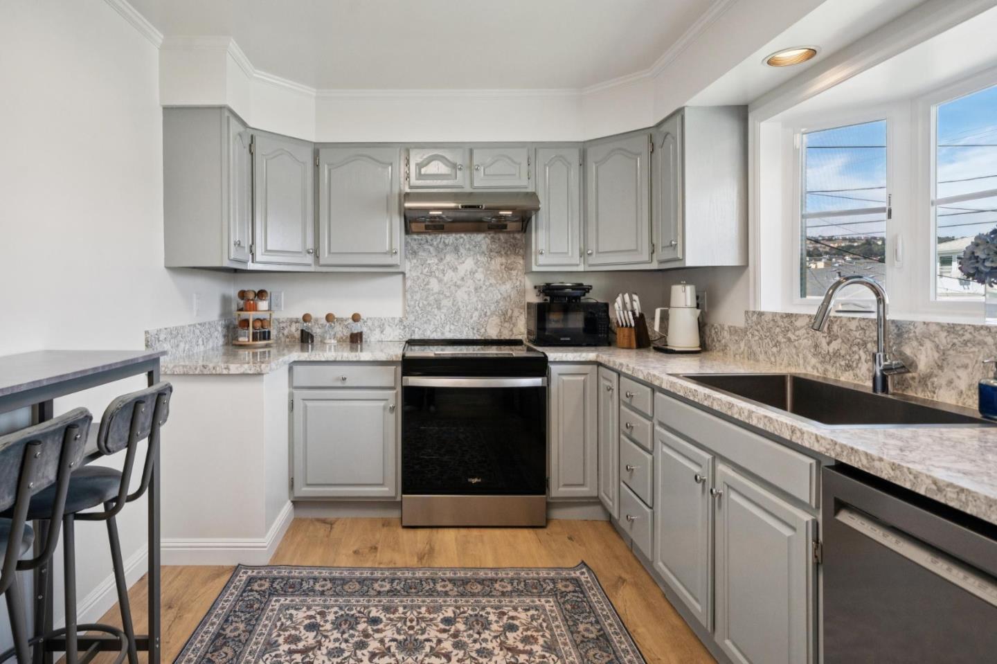 Kitchen with gray cabinets, marble-pattern counters, black range, and windows above the sink.