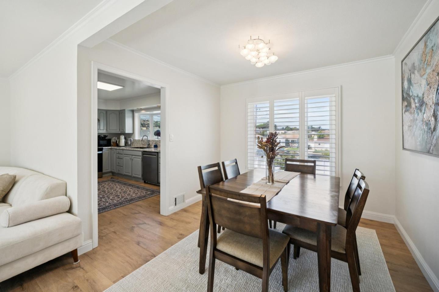 Dining room with dark wood table, plantation-shuttered windows, and an open doorway to the kitchen.