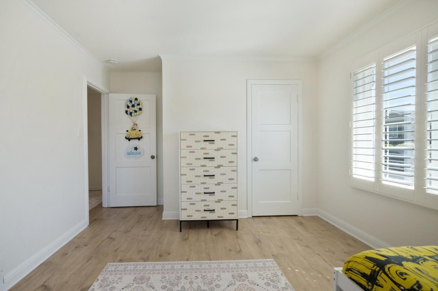 Bright bedroom with plantation shutters, a geometric-front dresser, and a yellow-and-black bedspread.