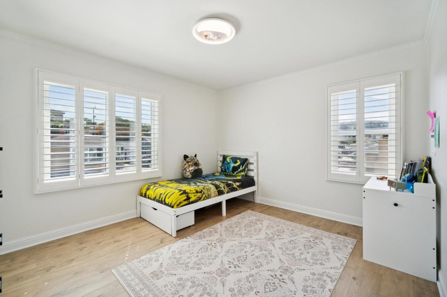 Furnished bedroom with a single bed, hardwood floors, and plantation-shuttered windows.