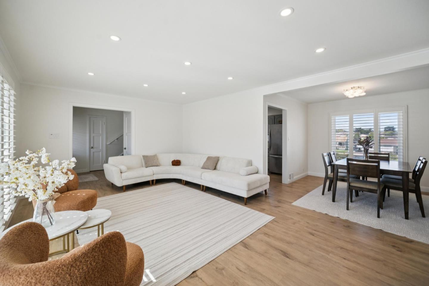 Open-plan living and dining room with a white sectional sofa and dining table beside shuttered windows.
