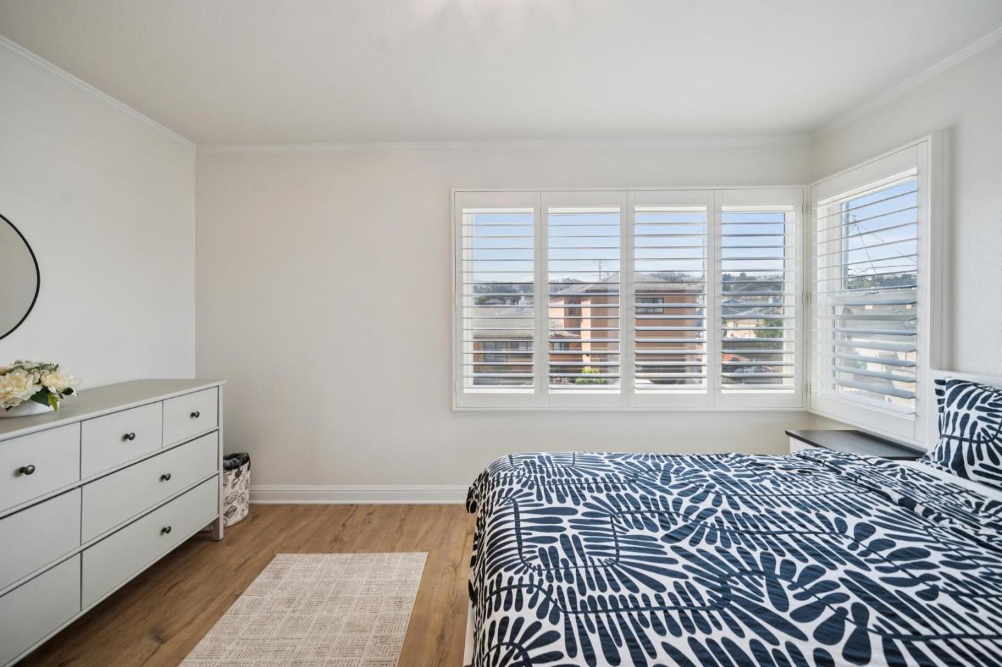 Bedroom with navy-and-white patterned bedding, broad shuttered windows, and a white dresser.