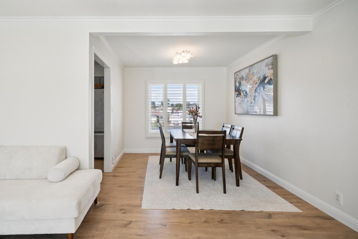 Dining room with a dark wood table, plantation shutters, hardwood floors, and a white sofa in the foreground.