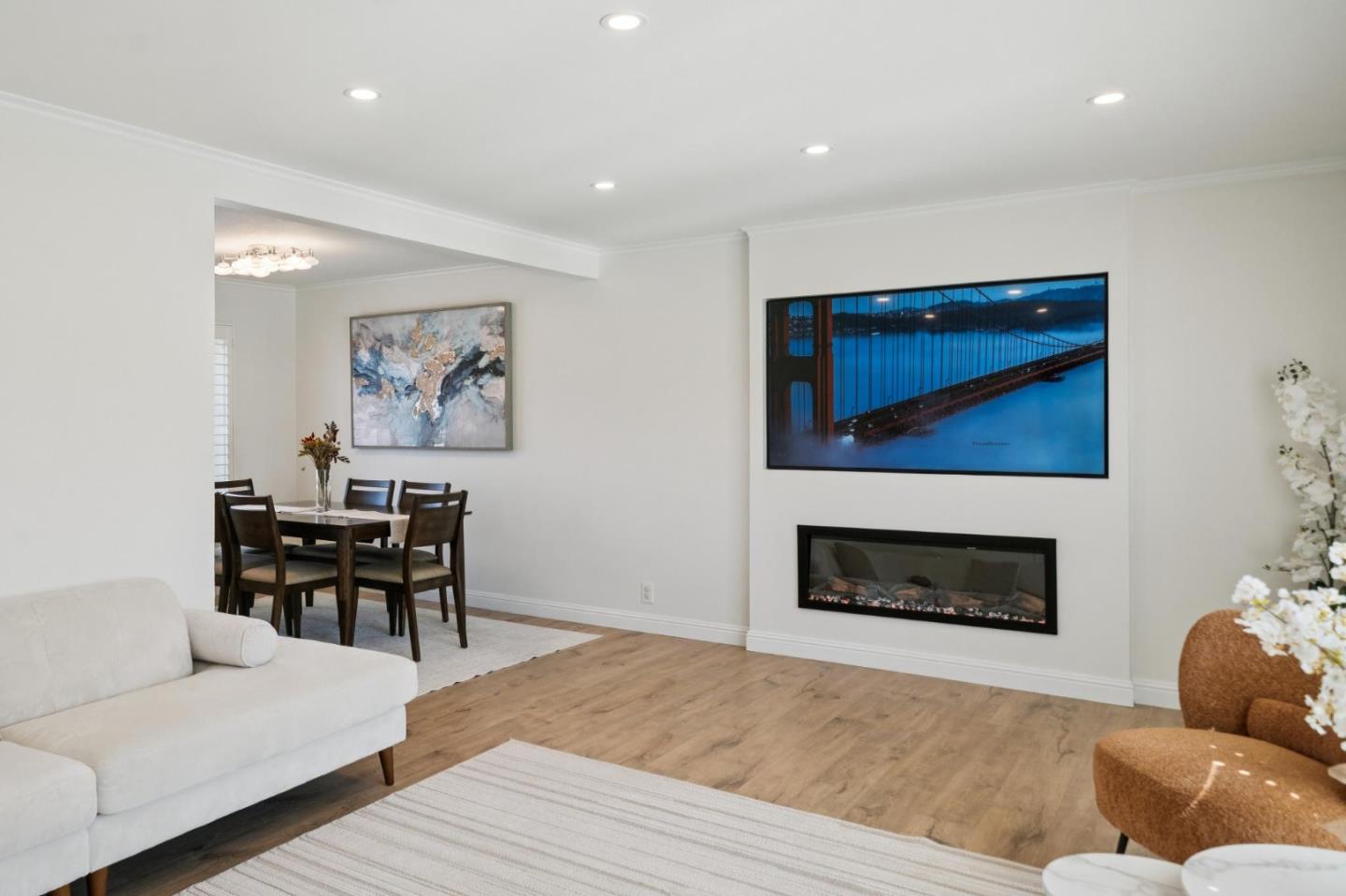 Living room with a white sofa, wall-mounted television, and built-in fireplace beside the dining area.