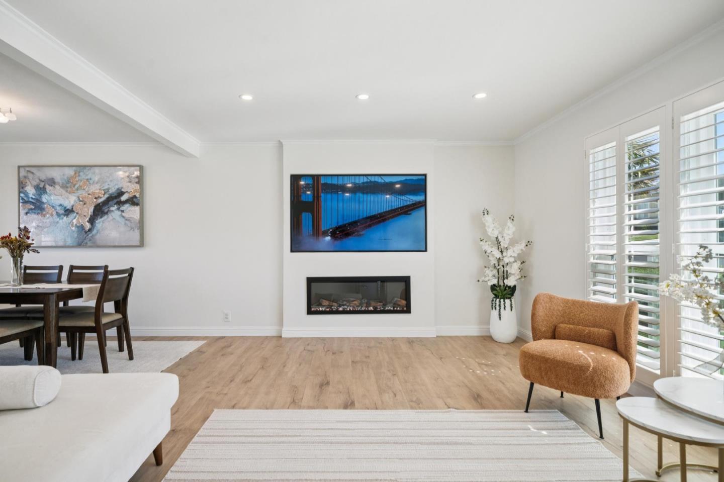 Furnished living room with a modern fireplace, plantation shutters, and a tan accent chair.