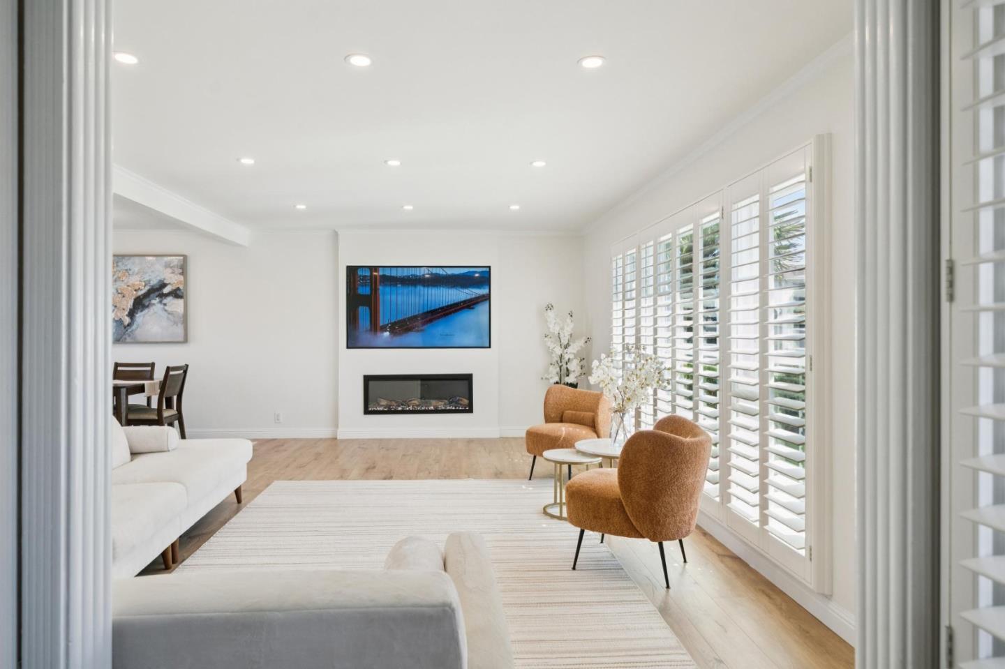 Furnished living room with rust-colored armchairs, plantation shutters, and a television above the fireplace.