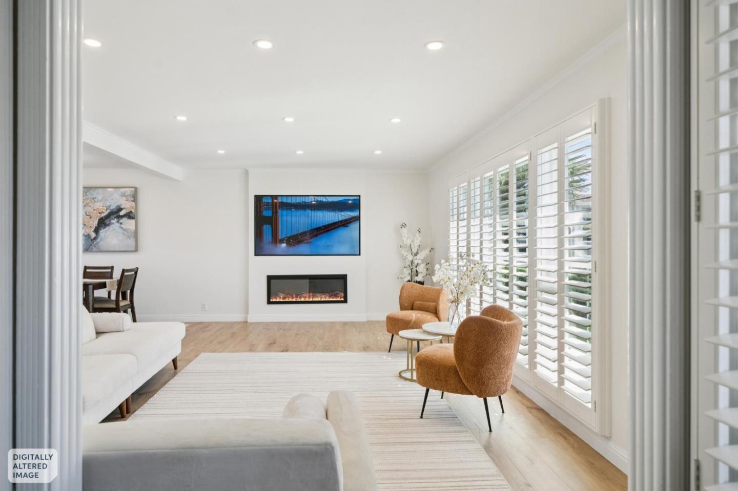 Bright staged living room with a linear fireplace, wall-mounted television, and plantation shutters.