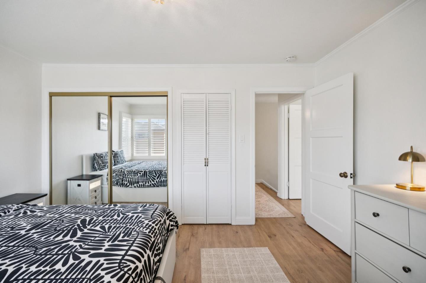 Bedroom with black-and-white patterned bedding, mirrored closet doors, and warm wood flooring.