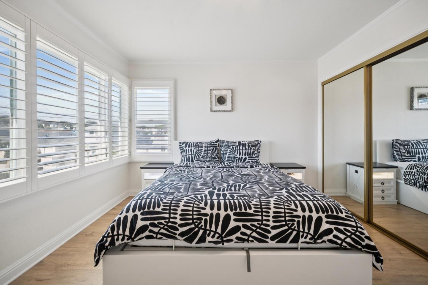 Bedroom with a black-and-white patterned bedspread, plantation shutters, and mirrored closet doors.