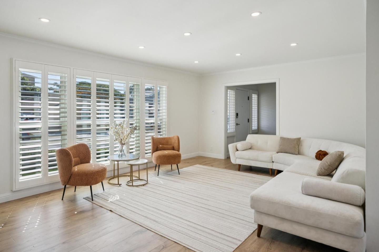 Living room with plantation shutters, a white sectional sofa, and two rust-colored accent chairs.