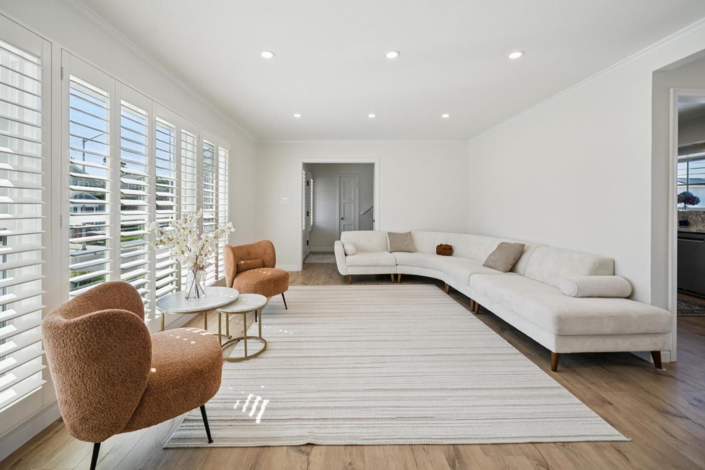 Living room with a white sectional, rust-colored chairs, and tall plantation-shuttered windows.
