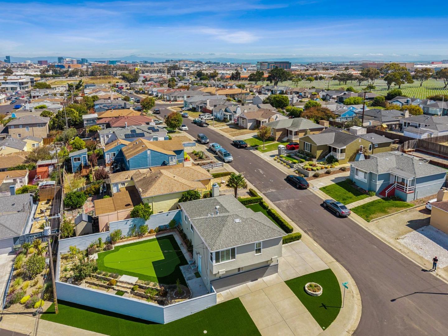 Aerial view of a two-story corner home with a landscaped yard and residential streets stretching toward distant buildings.