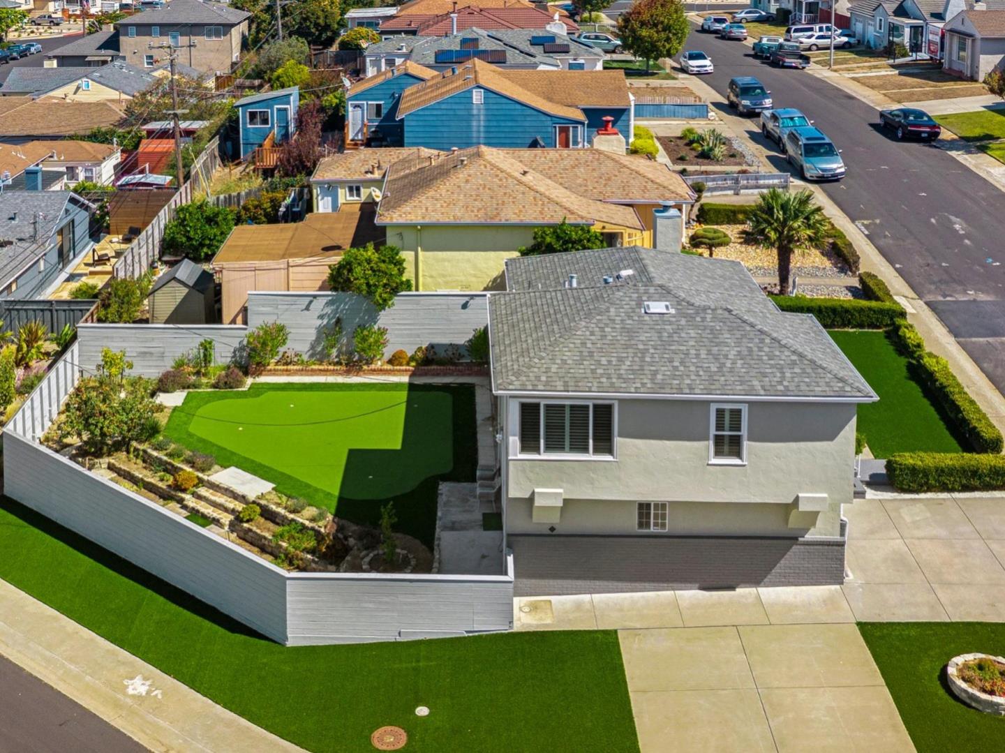 Aerial view of a gray house with a fenced artificial-turf yard and driveway.