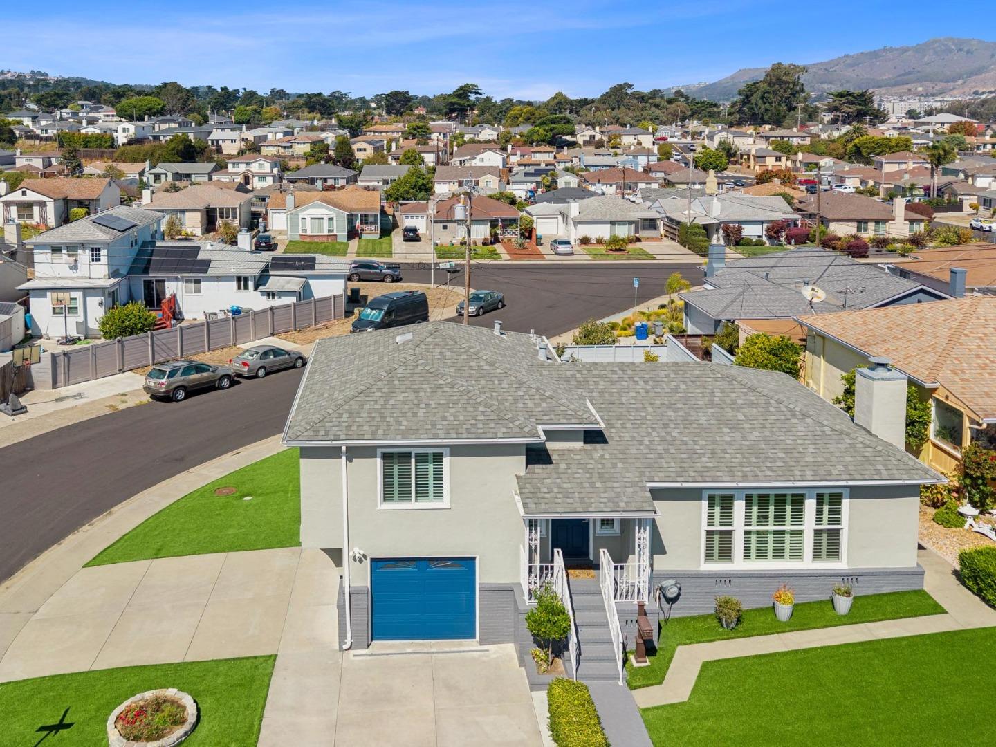 Aerial view of a gray home with a blue garage door, lawn, and surrounding neighborhood.