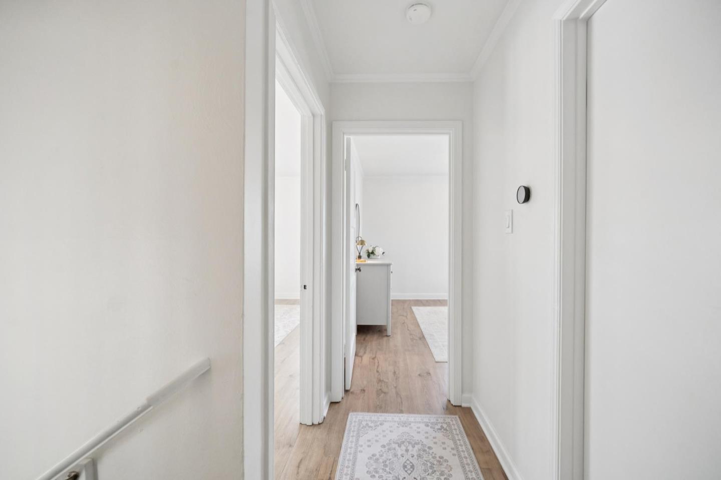 White hallway with light wood flooring, a patterned runner, and open doorways.