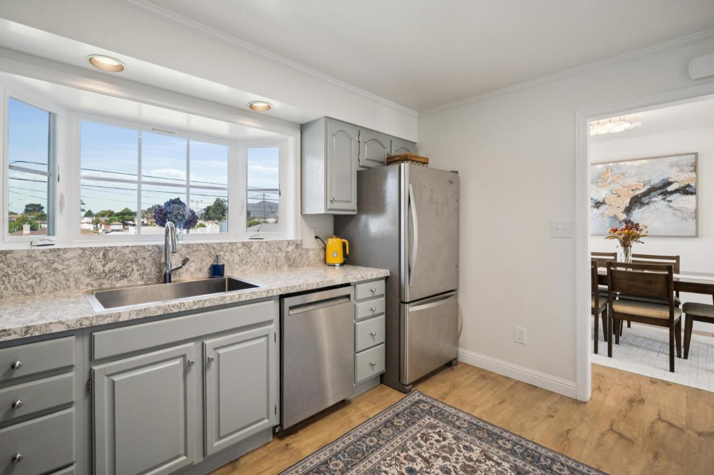 Kitchen with gray cabinets, stone counters, and large windows overlooking nearby homes.
