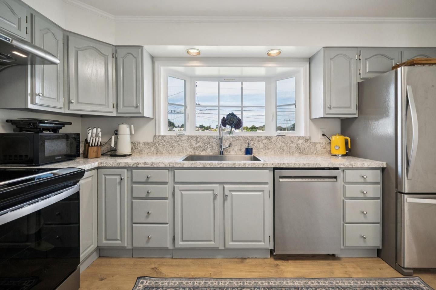 Kitchen with gray cabinets, stainless steel appliances, and a wide bay window above the sink.