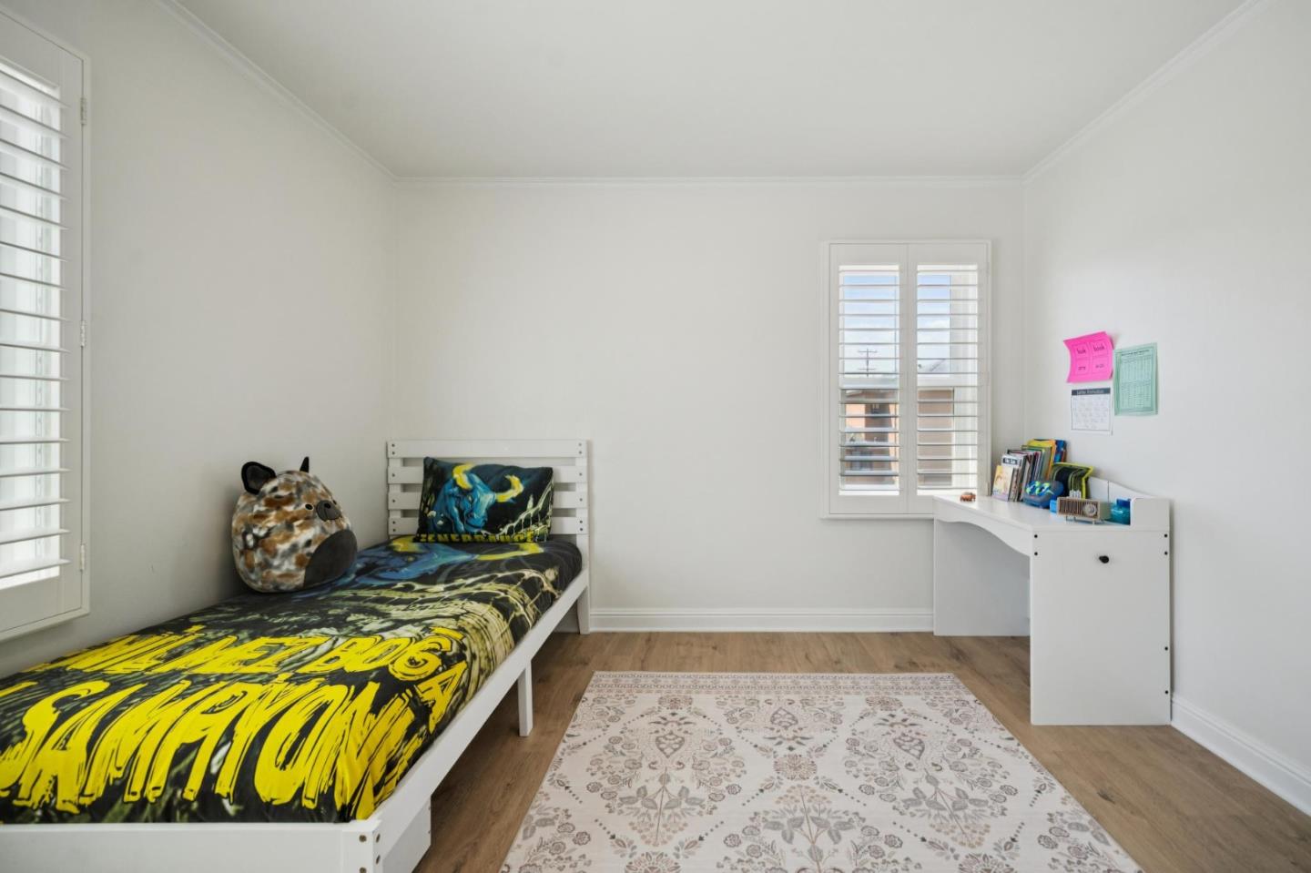Bedroom with a single bed, bold graphic bedding, plantation shutters, and a small desk.