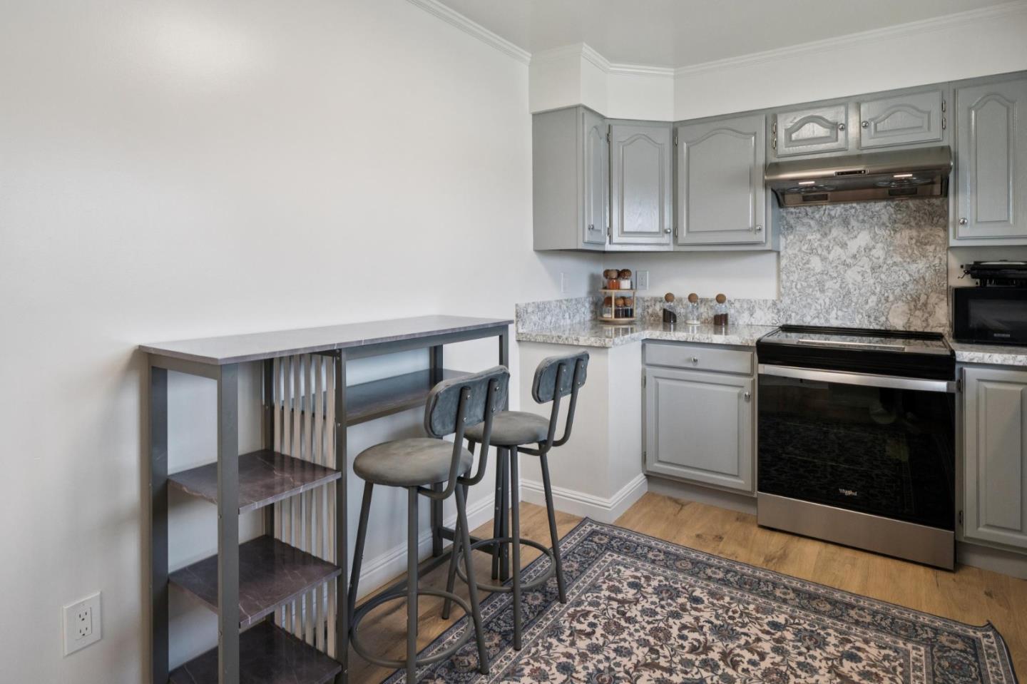 Kitchen with gray cabinets, a stainless steel range, and a narrow table with two stools.