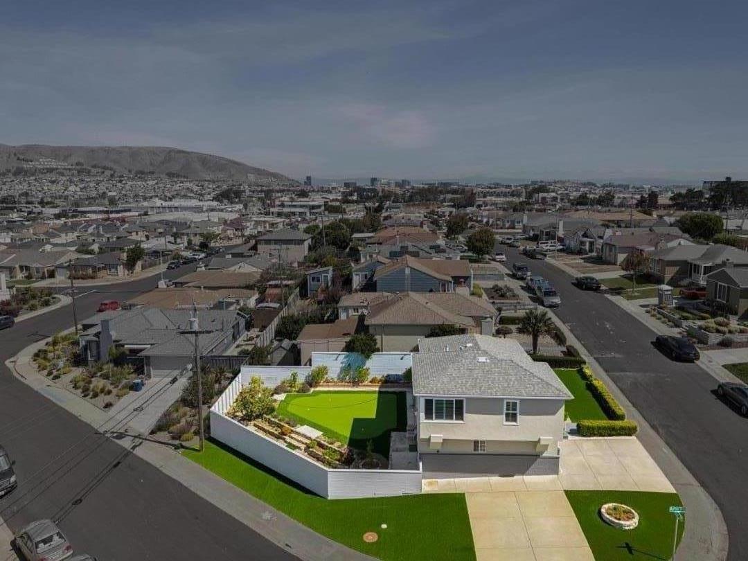 Aerial view of a two-story home with a walled green yard in a dense residential neighborhood.