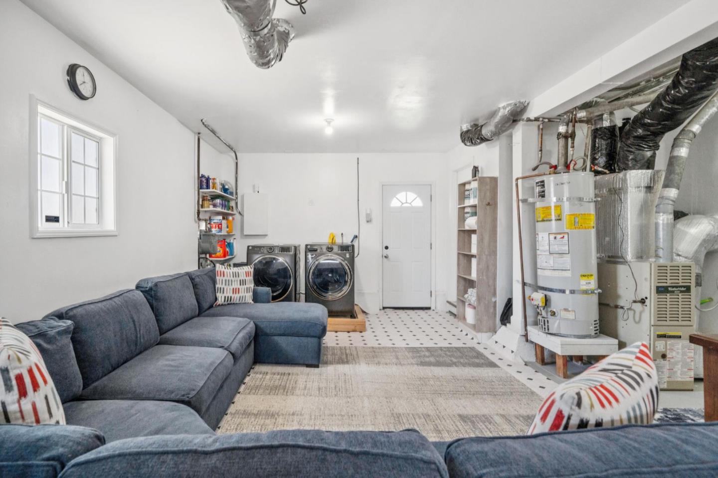 Furnished laundry and utility room with washer, dryer, blue sectional sofa, and exposed utility equipment.