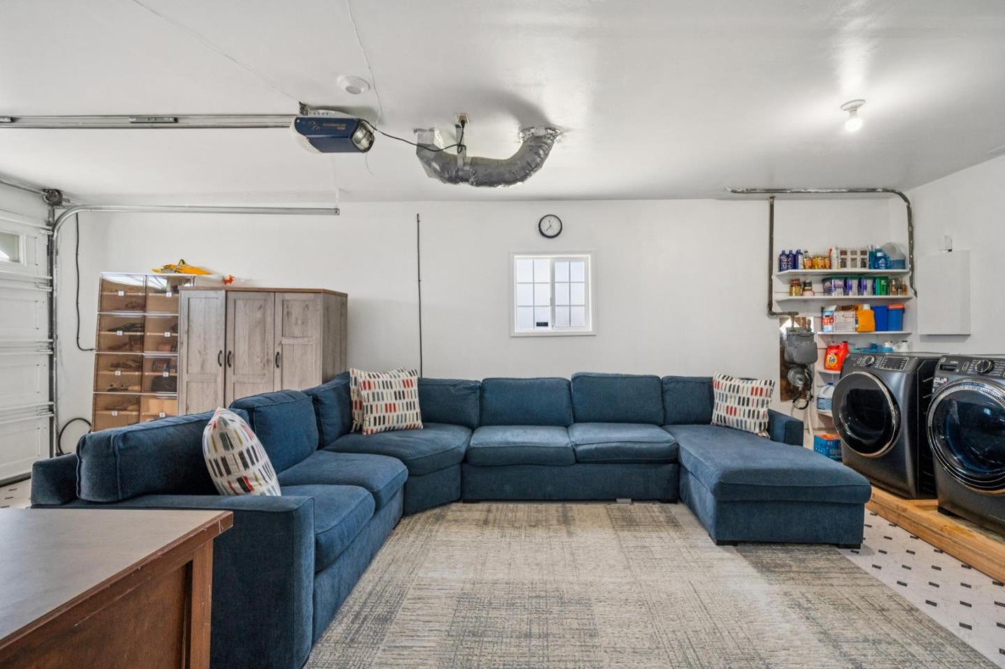 Garage furnished with a blue sectional, area rug, storage cabinets, and laundry machines.