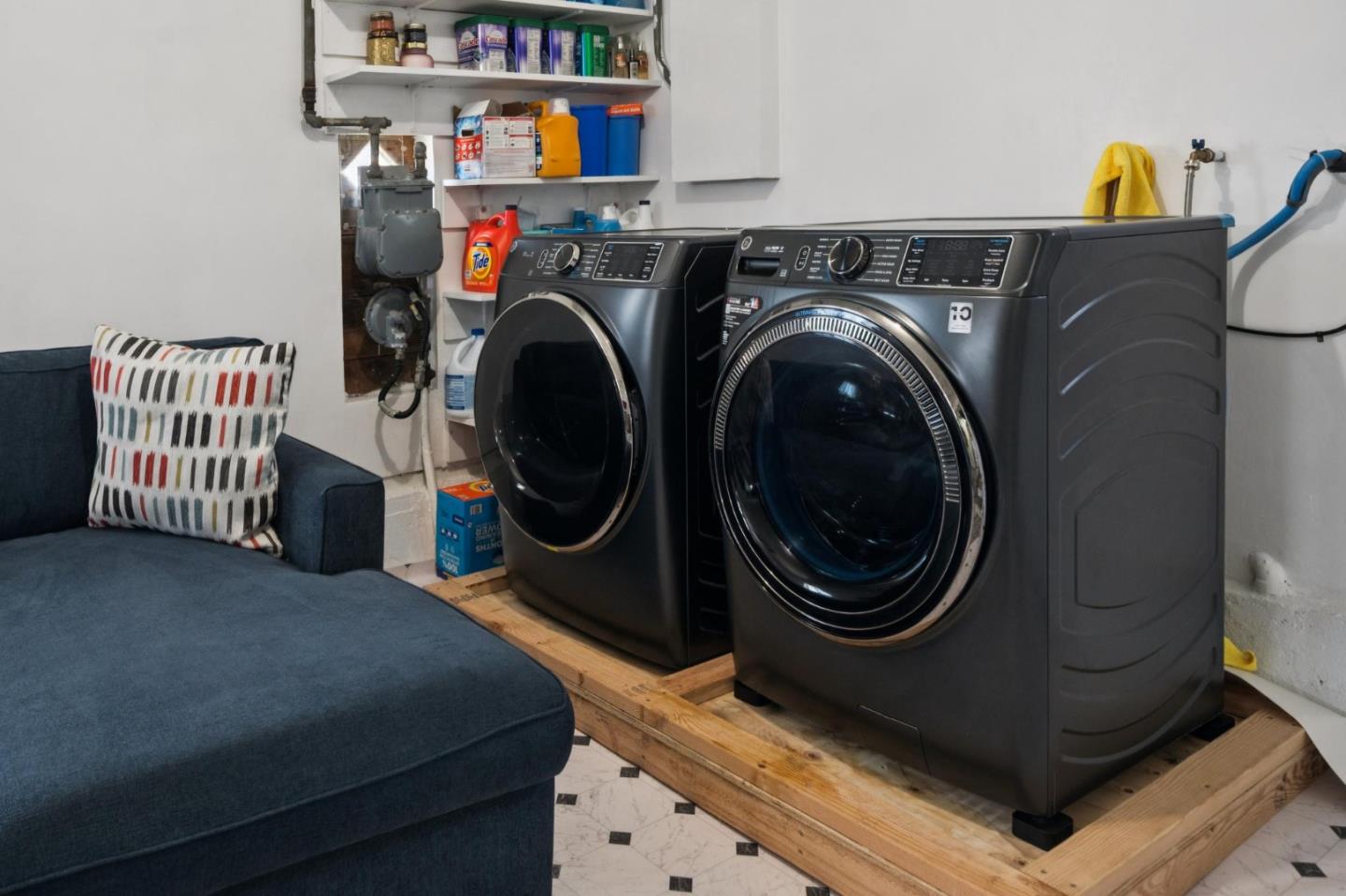 Laundry area with front-loading washer and dryer beside a blue sofa.