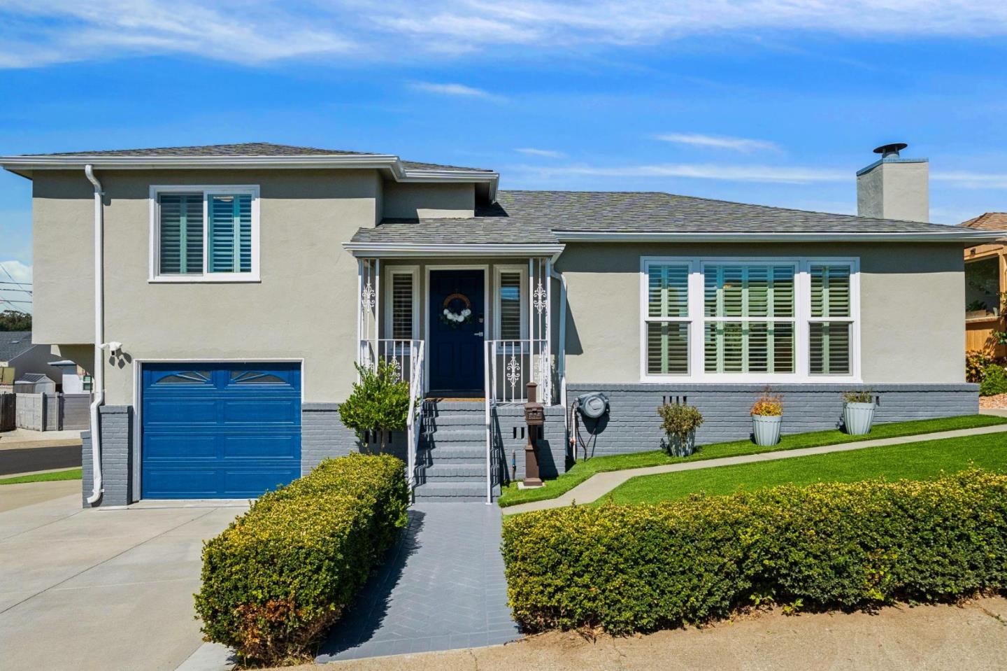 Front of a light stucco home with blue garage and entry doors, shuttered windows, and landscaped walkway.