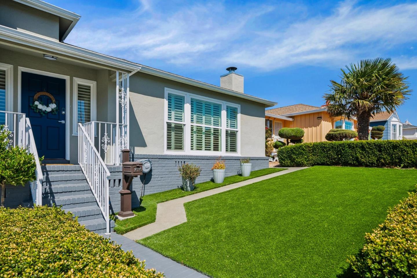 Gray home with a blue front door, white porch railings, and a broad green lawn.
