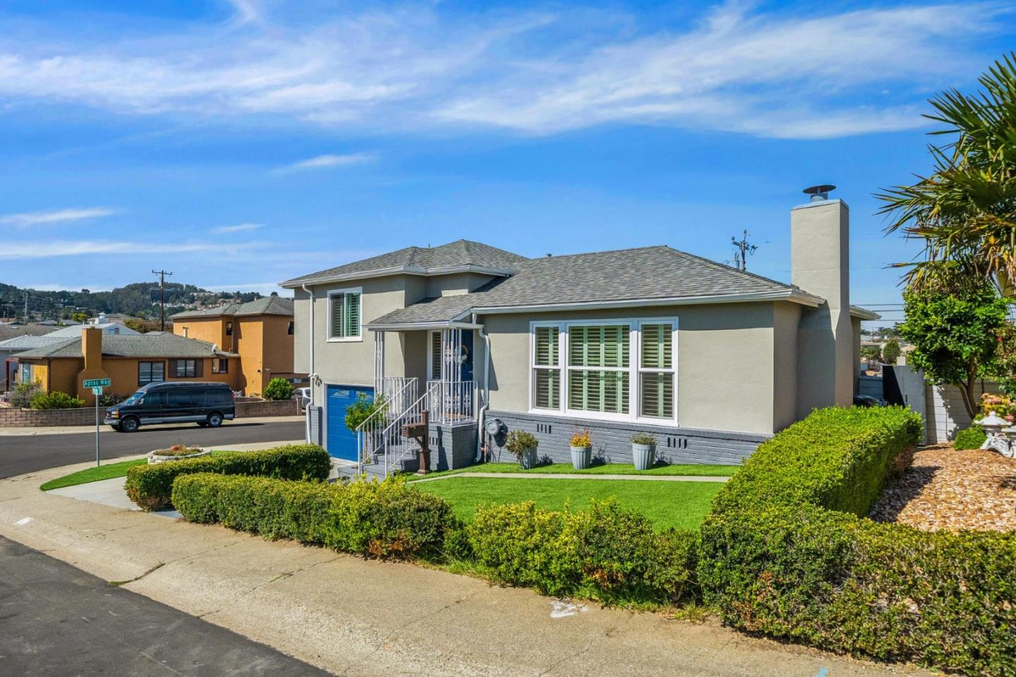Gray stucco house with a blue garage door, front lawn, and clipped hedges.