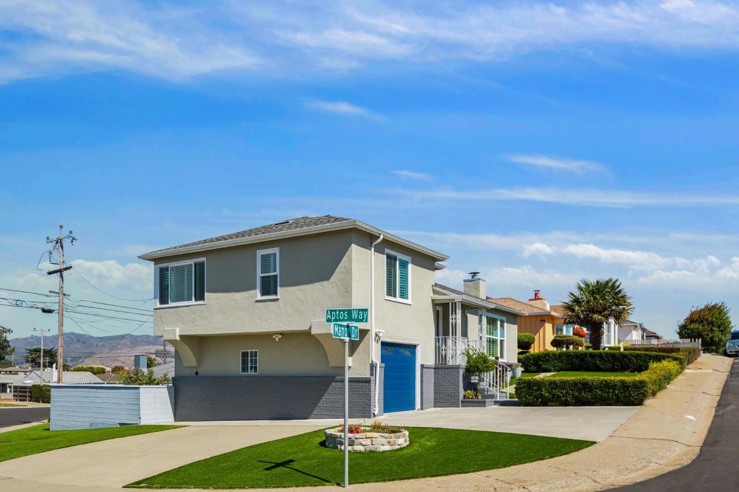 Two-story corner home with a blue garage door, trimmed hedges, and a green front lawn.