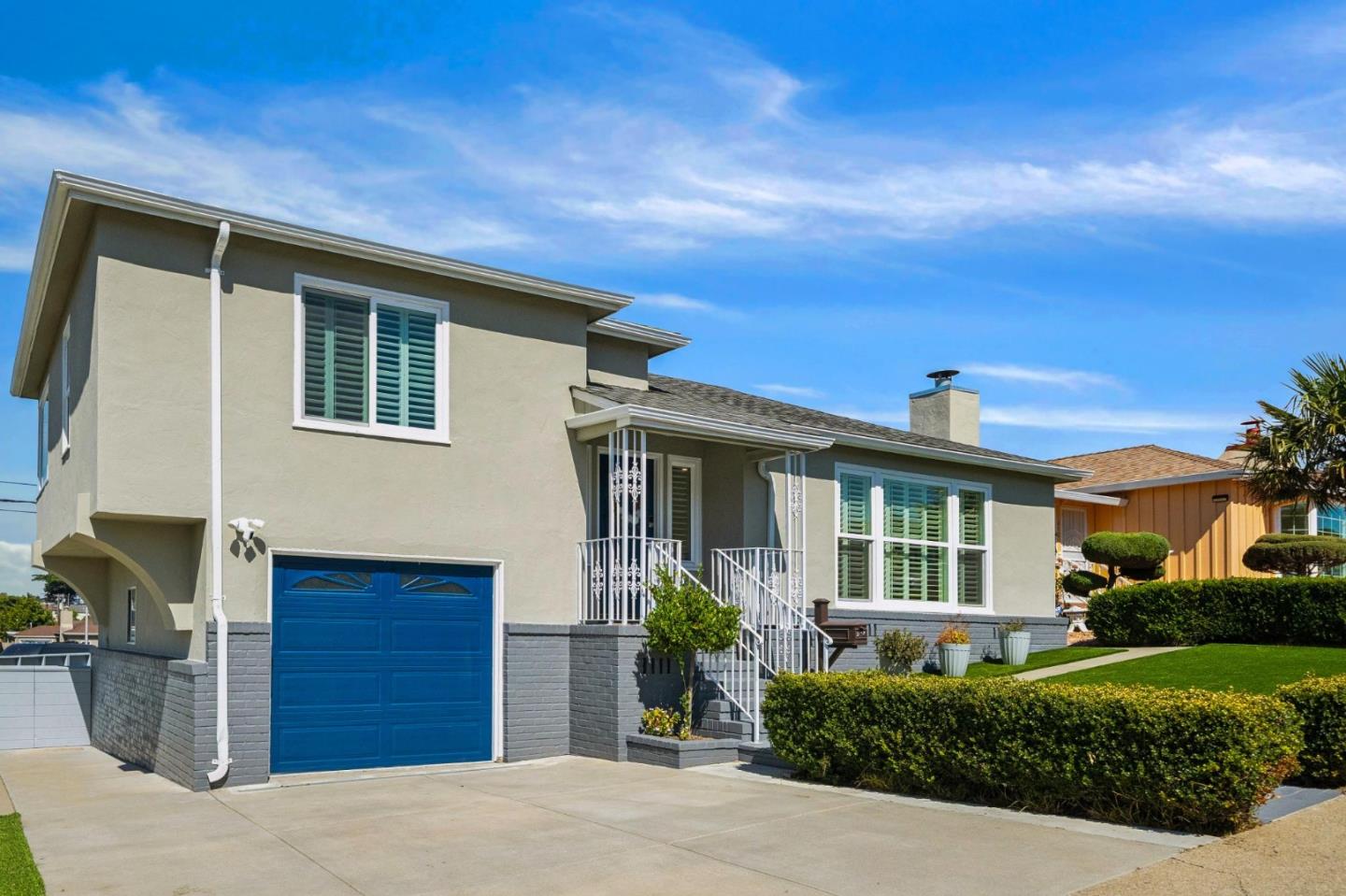 Stucco home with a bright blue garage door, white shutters, and trimmed front hedges.
