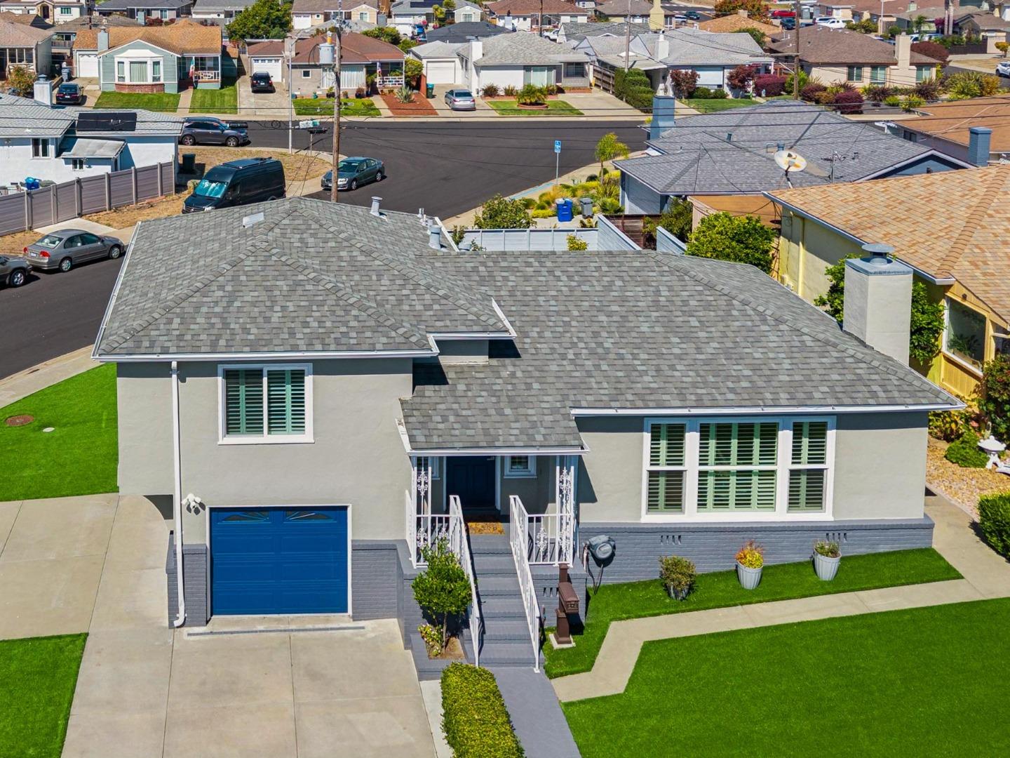 Gray single-story home with a broad shingle roof, blue garage door, and front lawn, viewed from above.